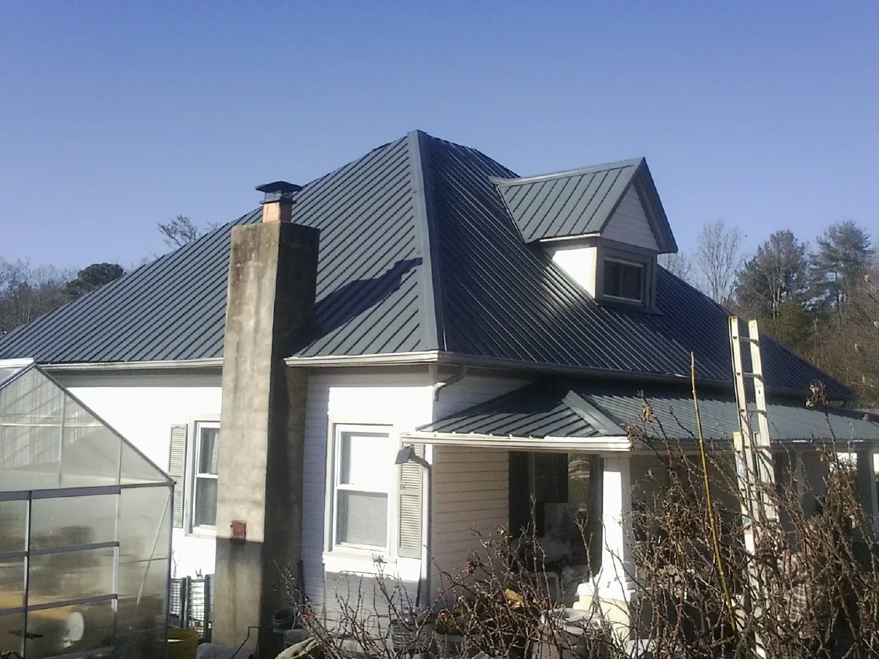 Dark blue standing seam metal roof on a white farmhouse with dormer — Slate & Tile Roof Repair by Roofing Brothers in Spraggs