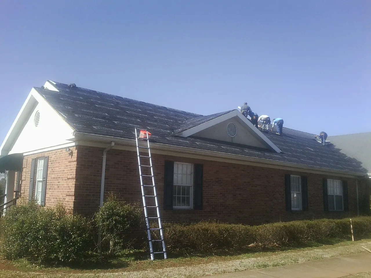 Crew tearing shingles off a brick ranch roof with a ladder set — Metal Roof Repair work by our crew in Spraggs