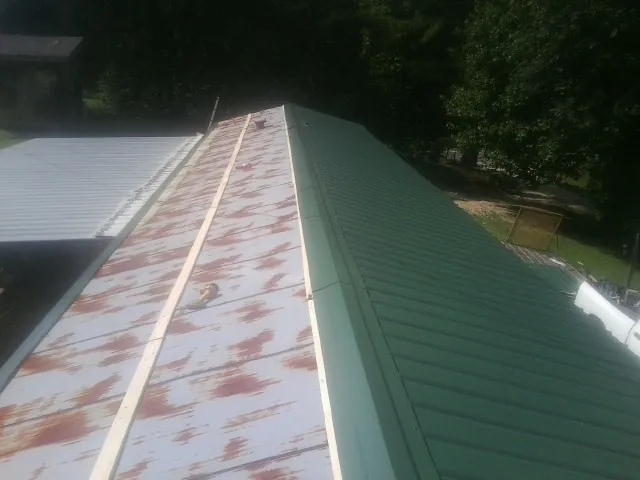 Old rusted panels beside newly installed green metal roofing — Wind Damage Roof Repair by Roofing Brothers in Spraggs