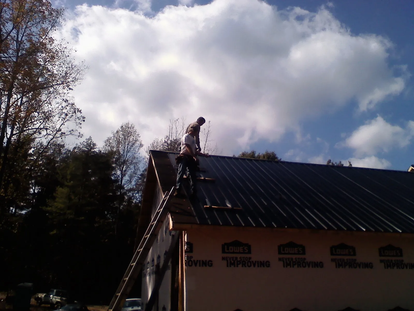 Roofer fastening dark metal panels high against a cloudy sky, from a Roof Inspection job in Spraggs