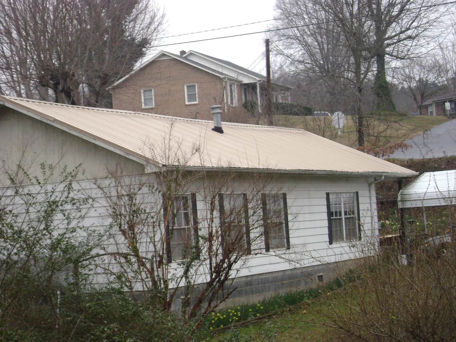 Tan metal roof on a white sided house set into a hillside — Commercial Roofing by Roofing Brothers in Spraggs