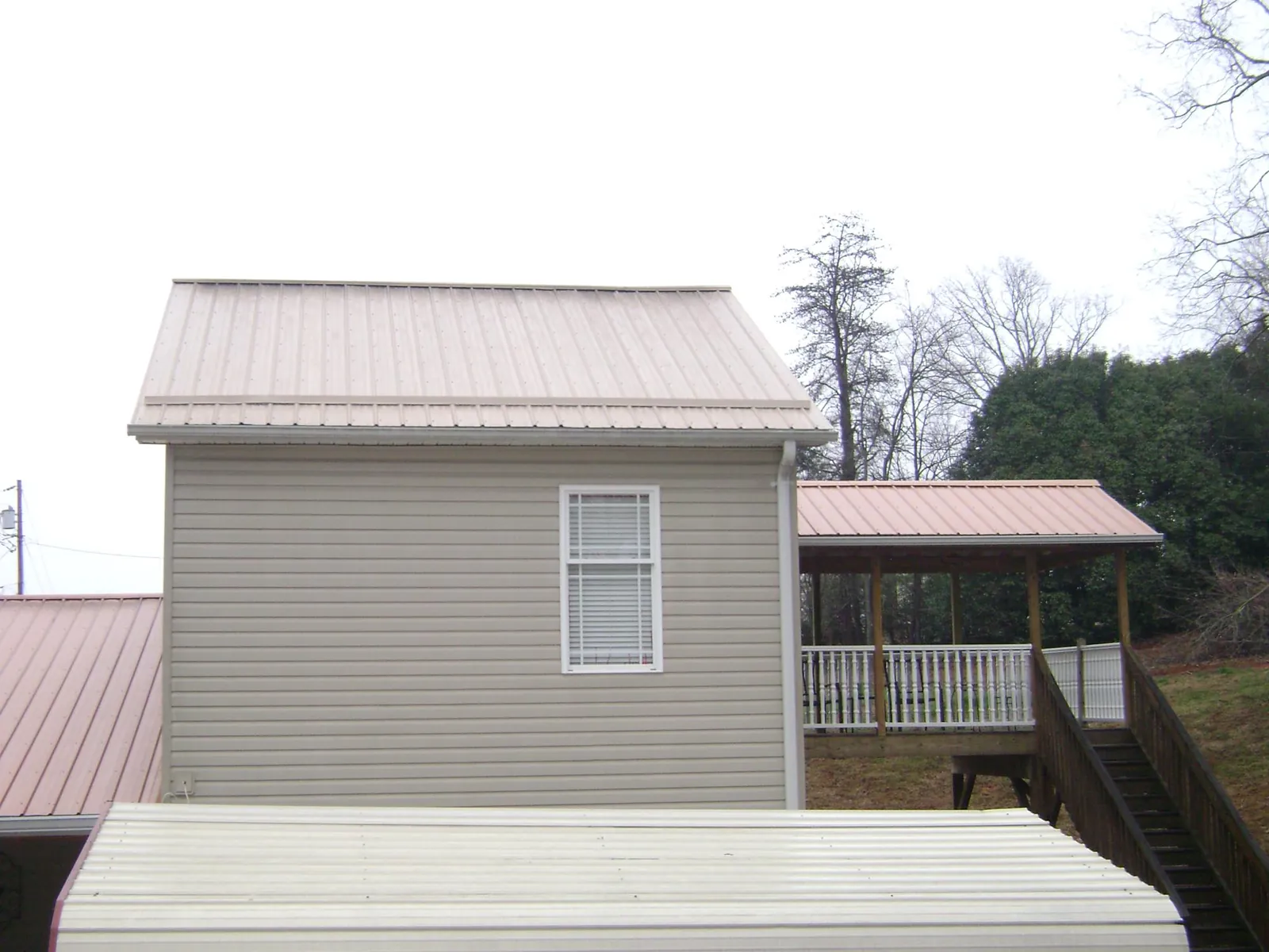 Tan metal roofs on a two story addition and attached porch, from a Roof Replacement job in Spraggs